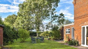 A well-maintained backyard with a grassy lawn, a wooden shed, and a brick building with a door. - 1 Brandiston Barn Cottage (Cawston near Reepham)