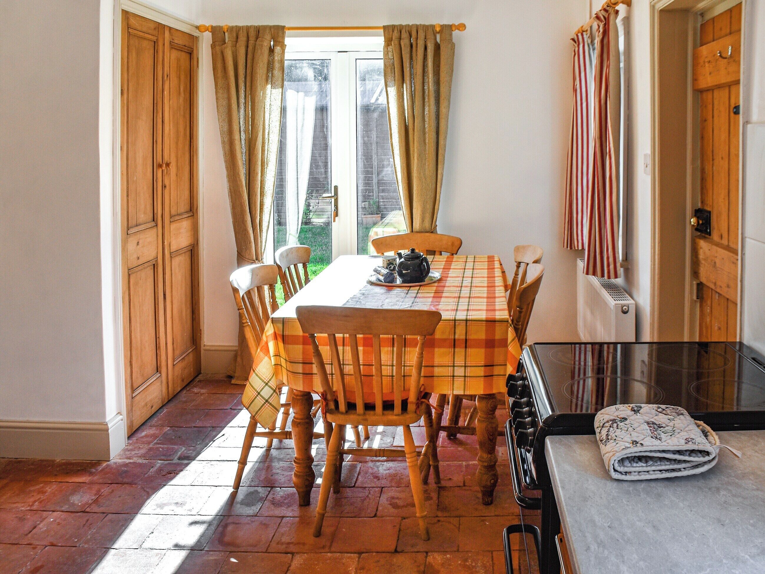 A dining area with a table set for four, wooden chairs, a plaid tablecloth, and a view through a glass door.