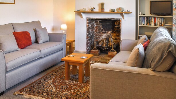 A living room with a fireplace, a sofa, a coffee table, and a bookshelf. - 1 Brandiston Barn Cottage (Cawston near Reepham)