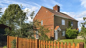A two-story house with a brick exterior and a wooden fence in front. - 1 Brandiston Barn Cottage (Cawston near Reepham)