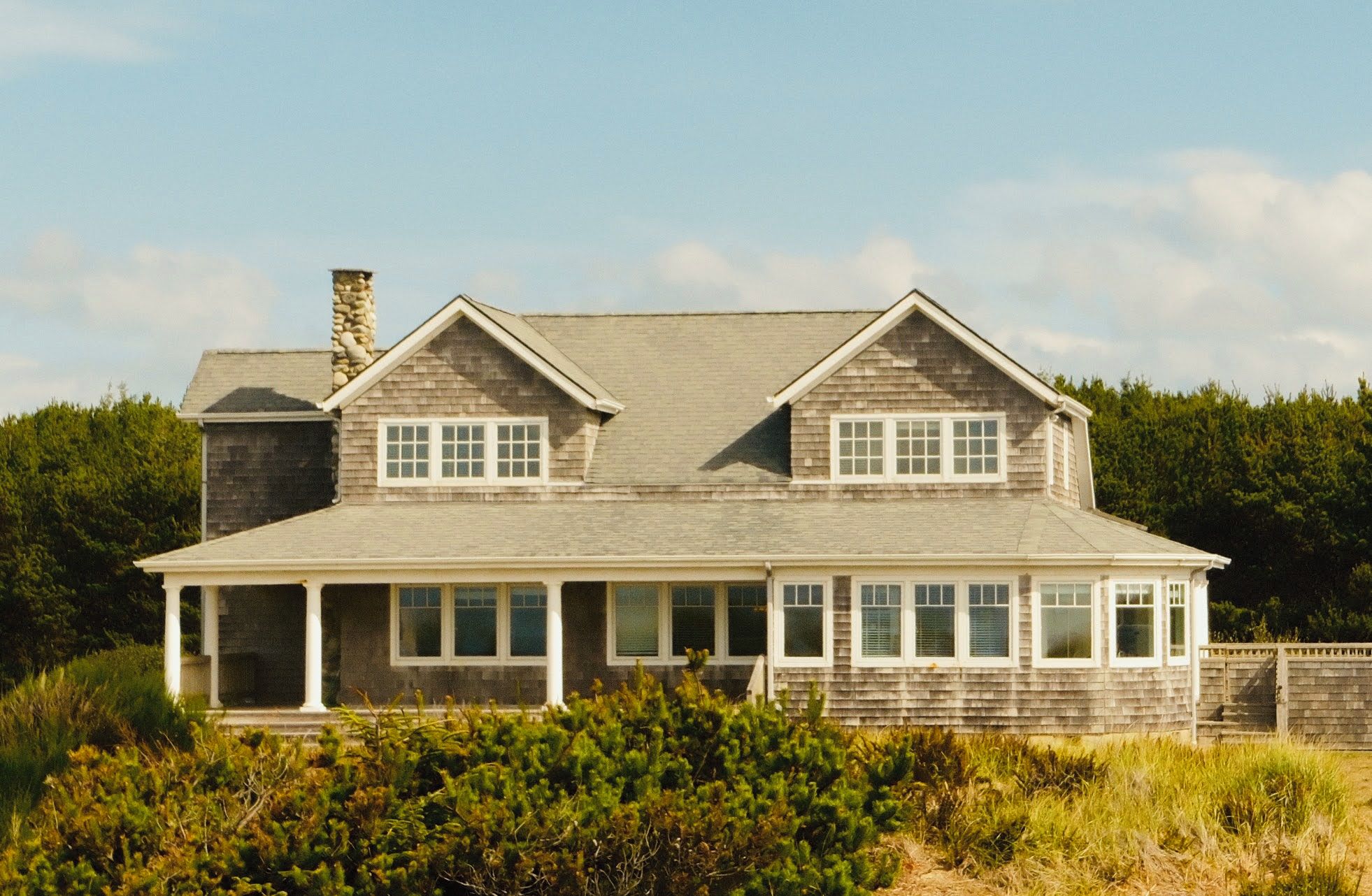 A two-story house with a gabled roof, a chimney, and a covered porch with multiple windows.