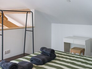 A room with a bunk bed, a desk, a small wooden table, and a patterned bedspread.