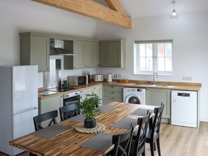 Una cocina moderna con vigas de madera, una mesa de comedor con sillas, un lavabo, un microondas, un tostador, un refrigerador y una lavadora.