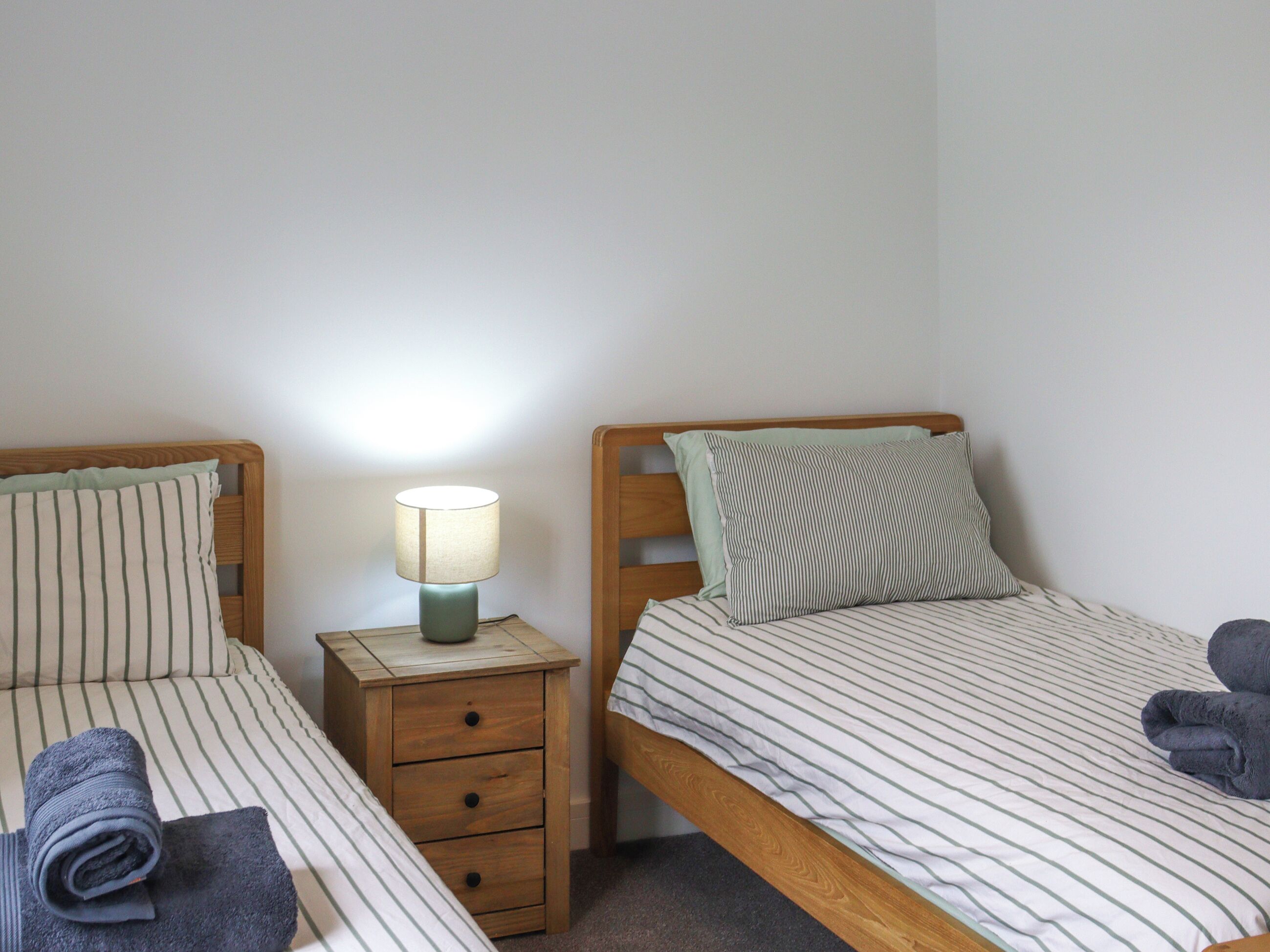 Zwei Einzelbetten mit gestreifter Bettwäsche, ein Nachttisch mit Lampe und ein Holz-Kopfteil.