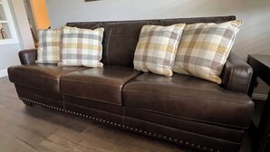 A brown leather sofa with plaid cushions, a wooden floor, and three framed pictures on the wall.