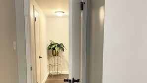 A hallway with wooden flooring and white walls, leading to a room with a door.
