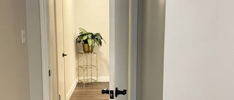 A hallway with wooden flooring and white walls, leading to a room with a door.