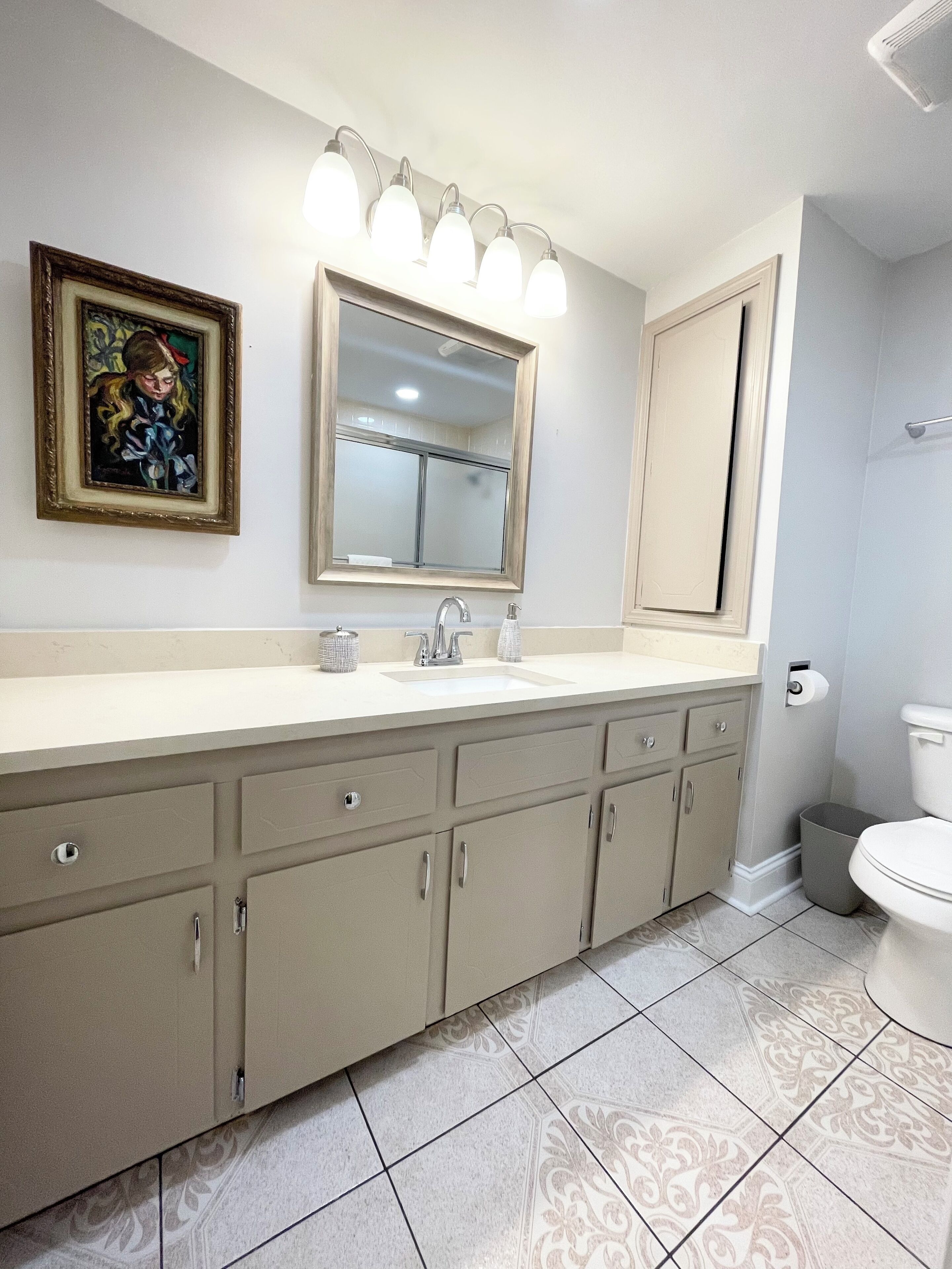 A bathroom with a large vanity, a mirror, a sink, and a toilet.