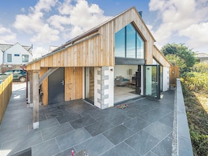 A modern house with a wooden exterior, a large glass window, and a stone pathway. - The Old Coach Garage (Gerrans)