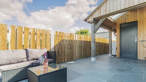 An outdoor patio with a sofa, a glass-top table, and a wooden fence. - The Old Coach Garage (Gerrans)