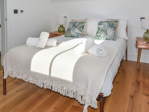 A neatly made bed with a white cover, two bedside tables with lamps, and a wooden floor. - The Old Coach Garage (Gerrans)