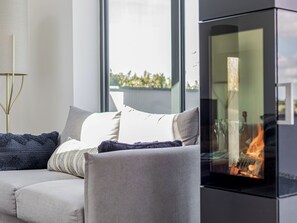 A modern living room with a sofa, cushions, a glass fireplace, and a large window. - The Old Coach Garage (Gerrans)