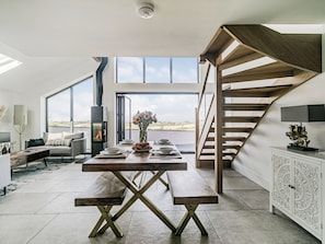 A modern interior with a dining table, benches, a fireplace, and a staircase.
