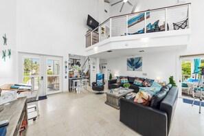 Uma sala de estar espaçosa com um sofá de couro preto, uma mesa de jantar e uma cozinha ao fundo.