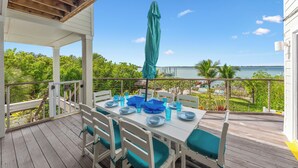 A covered outdoor dining area with white tables and chairs, a green umbrella, and a view of the ocean. - Gardens @ Bathtub Beach: 6BR/3BA Ocean2River, Pool, Spa, Elevator, Dock, Beach! (Stuart)