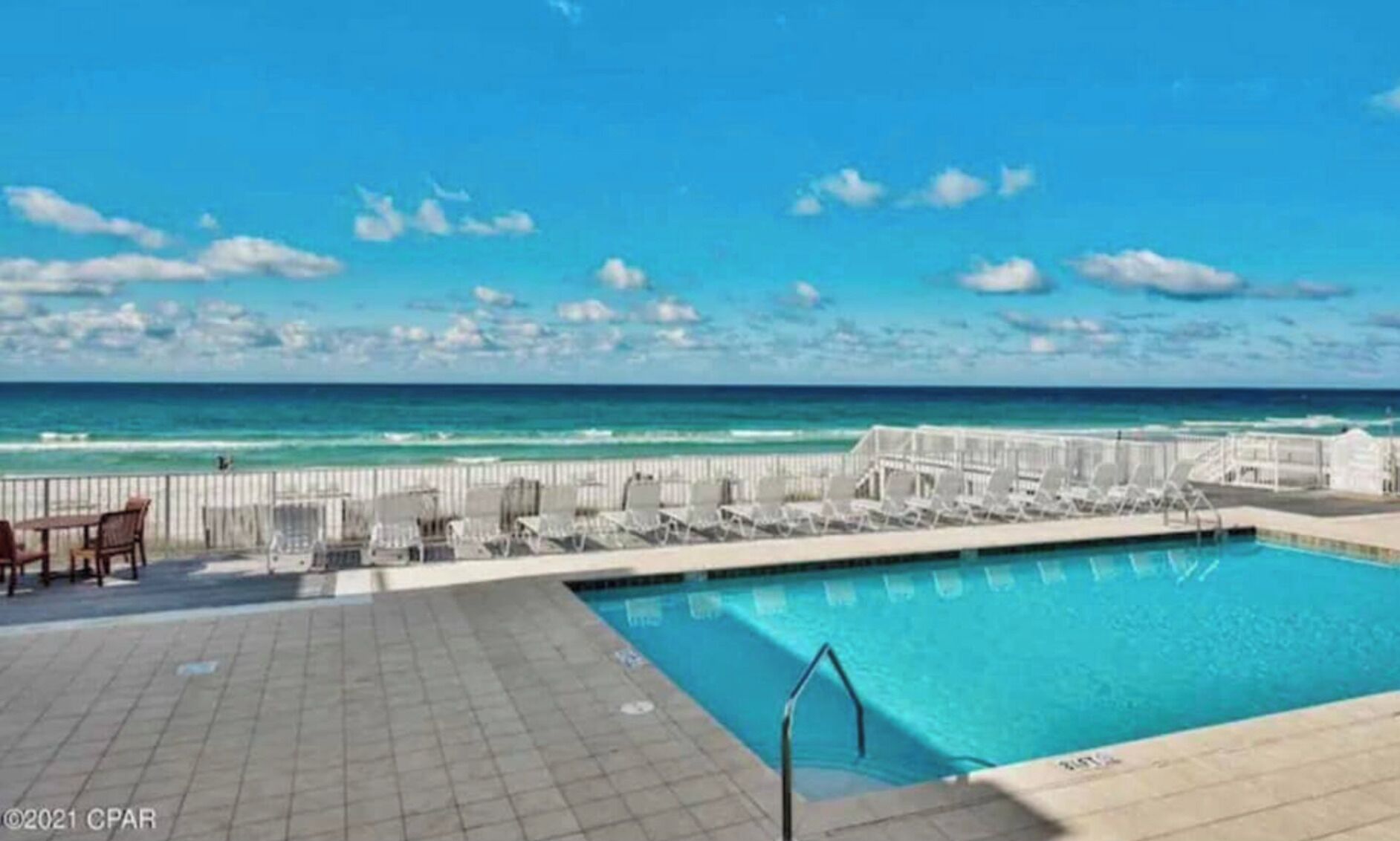 Ein Poolbereich mit Blick aufs Meer, eine umzäunte Terrasse mit Liegestühlen und ein gefliester Weg.