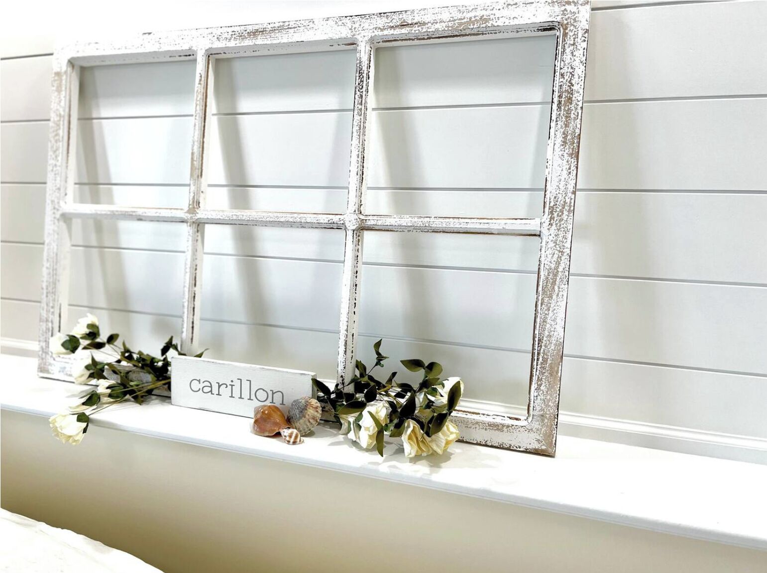 A white-framed window with a nameplate reading "Carillon" and a wreath of white flowers and green leaves.