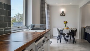 Een moderne keuken met een houten aanrecht, een ingebouwde wasmachine, een eethoek met tafel en stoelen, en een raam met uitzicht.