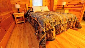 A wooden cabin bedroom with a bed, two nightstands, and a window. - Cabins at Pine Haven (Beaver)