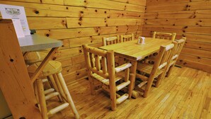 A wooden cabin with a dining table and chairs, a small counter, and a wooden floor. - Cabins at Pine Haven (Beaver)
