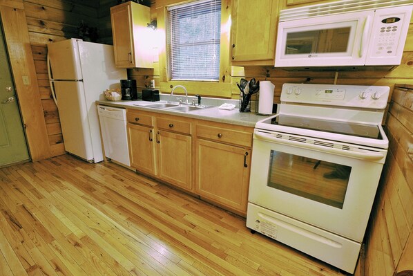 A kitchen with wooden cabinets, a refrigerator, a microwave, a stove, and a dishwasher. - Cabins at Pine Haven (Beaver)