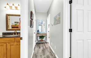 Enter a serene hallway leading to a bathroom with a sink, mirror, and potted plant.