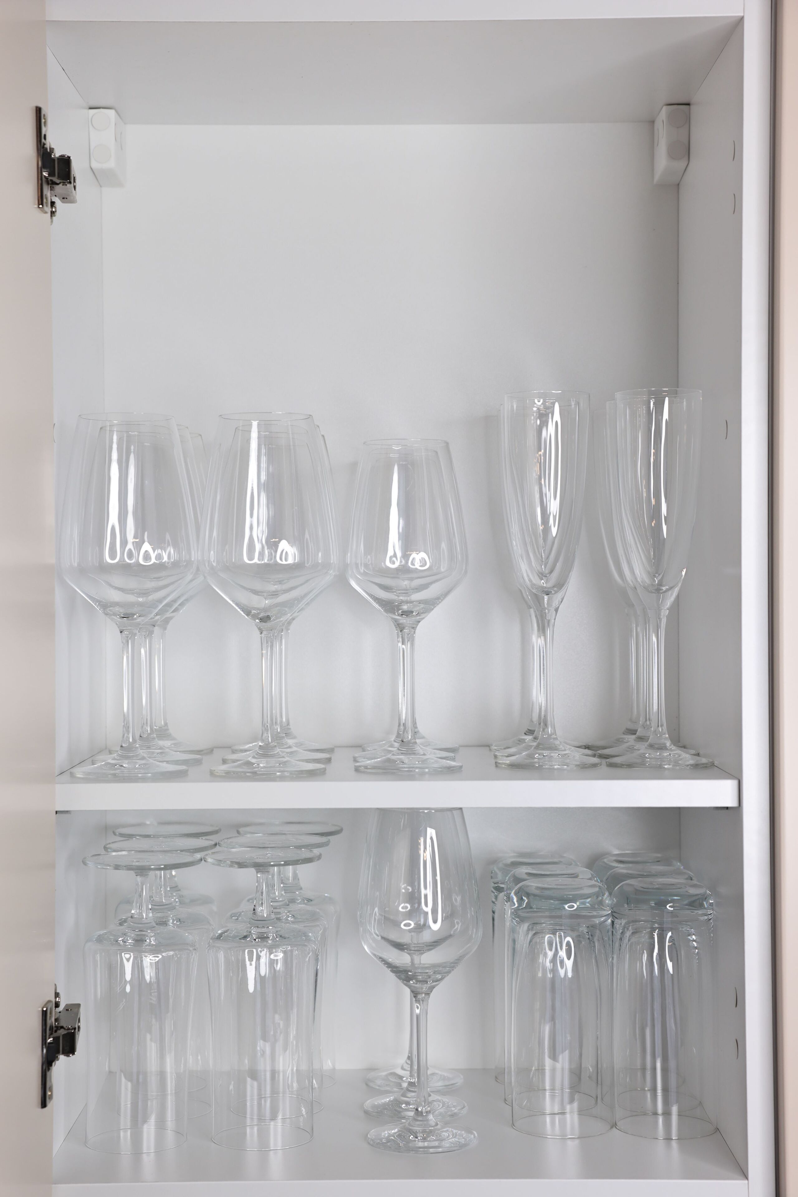Un meuble blanc contenant de la verrerie transparente, notamment des verres à vin et des verres à cocktail, disposés sur des étagères.