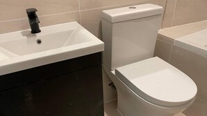 Une salle de bain avec un lavabo blanc, un meuble sombre et des toilettes blanches.