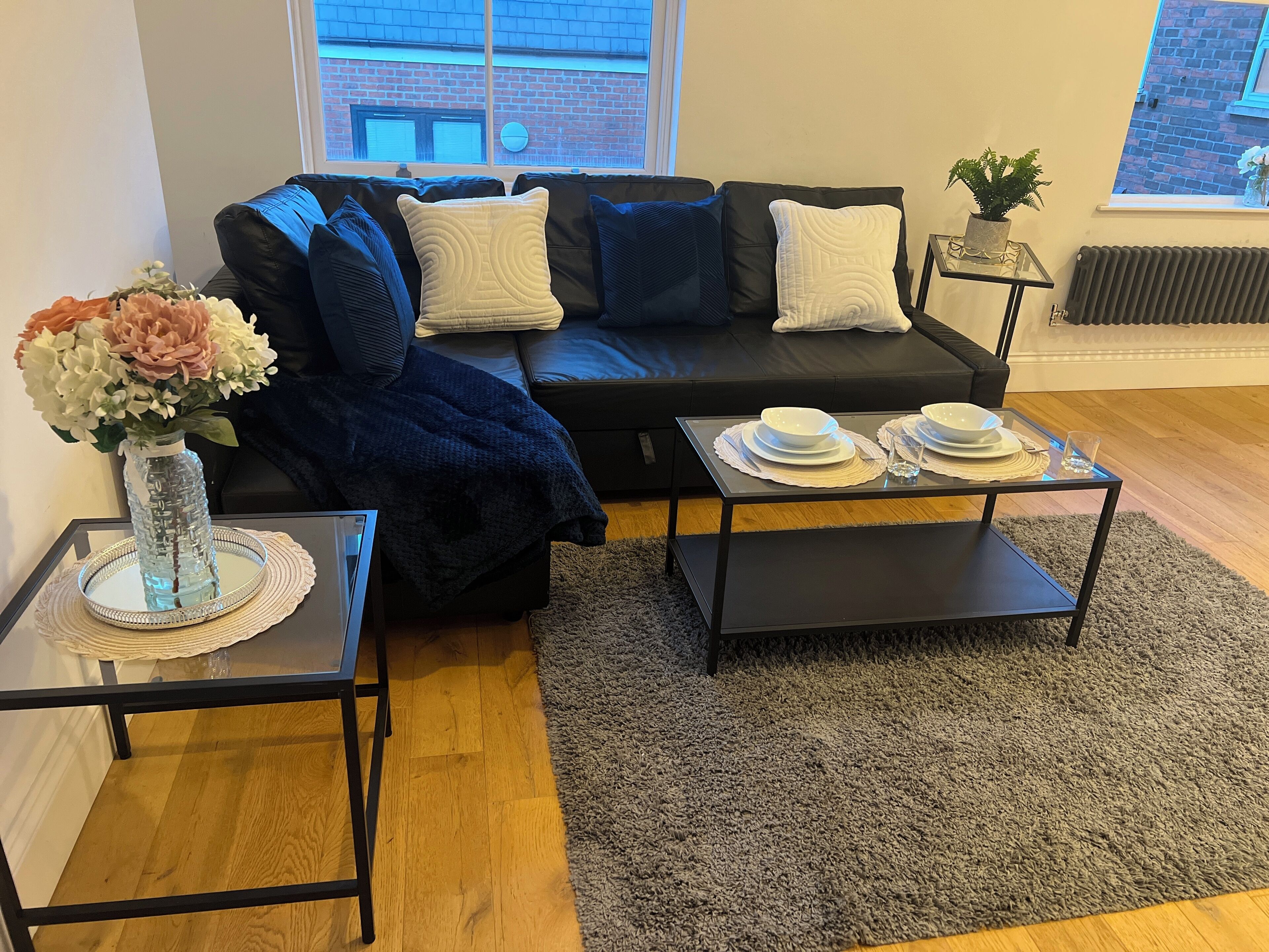A modern living room with a black sofa, a glass coffee table, and a small side table with a vase of flowers.
