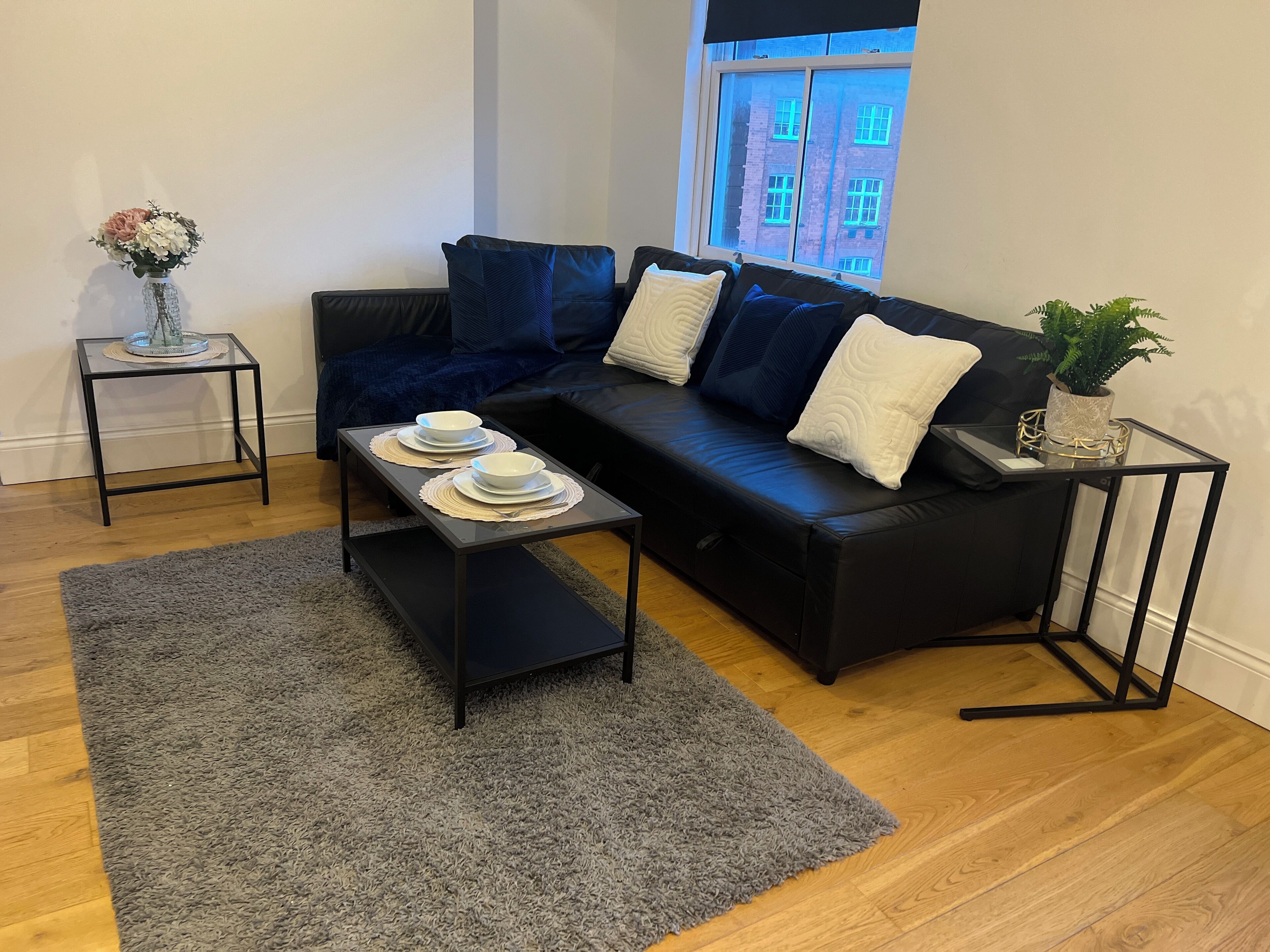 A modern living room with a black sofa, a glass coffee table, and a grey rug.