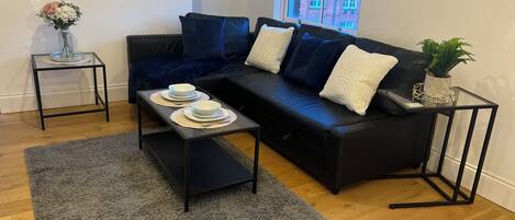 A modern living room with a black sofa, a glass coffee table, and a grey rug.