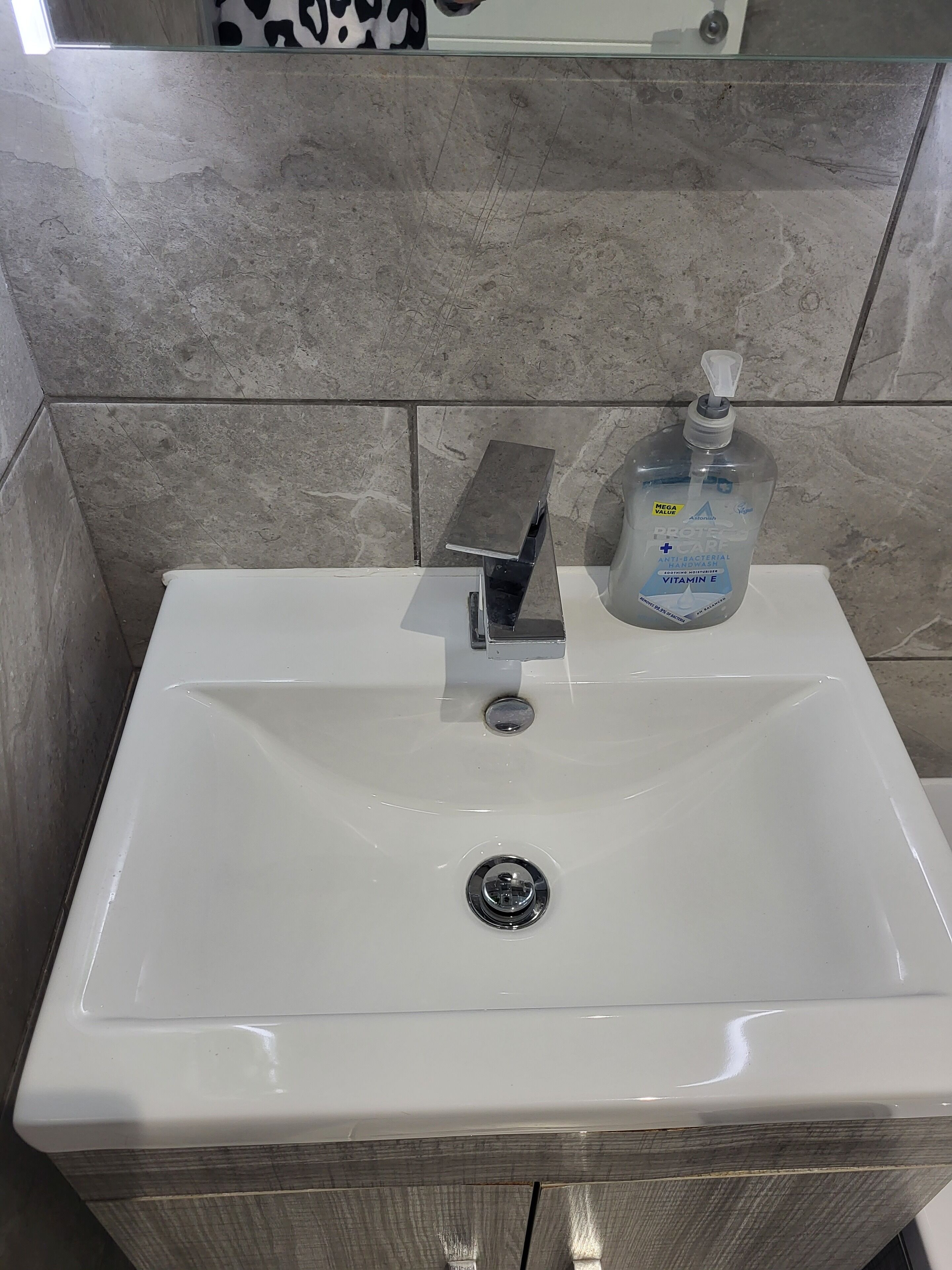 A bathroom sink with a soap dispenser, a mirror above it, and tiled walls.