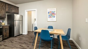 A modern kitchen with dark wooden cabinets, a stainless steel refrigerator, and a wooden dining table with blue chairs.