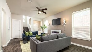 A modern living room with a grey sofa, a blue couch, and a ceiling fan.