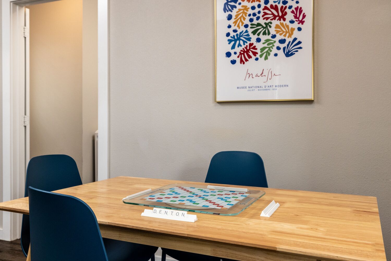 A conference room with a wooden table, two blue chairs, a framed artwork on the wall, and a nameplate on the table.