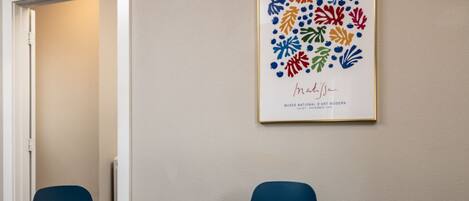 A conference room with a wooden table, two blue chairs, a framed artwork on the wall, and a nameplate on the table.