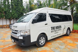 A white van with "The Haven Boutique Hotel Kumasi" branding parked on a stone-paved area.