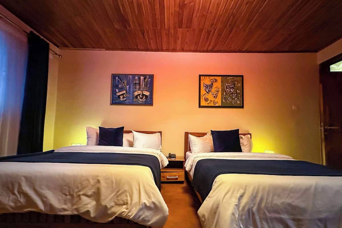 Habitación con dos camas, techo de madera y dos cuadros en la pared.