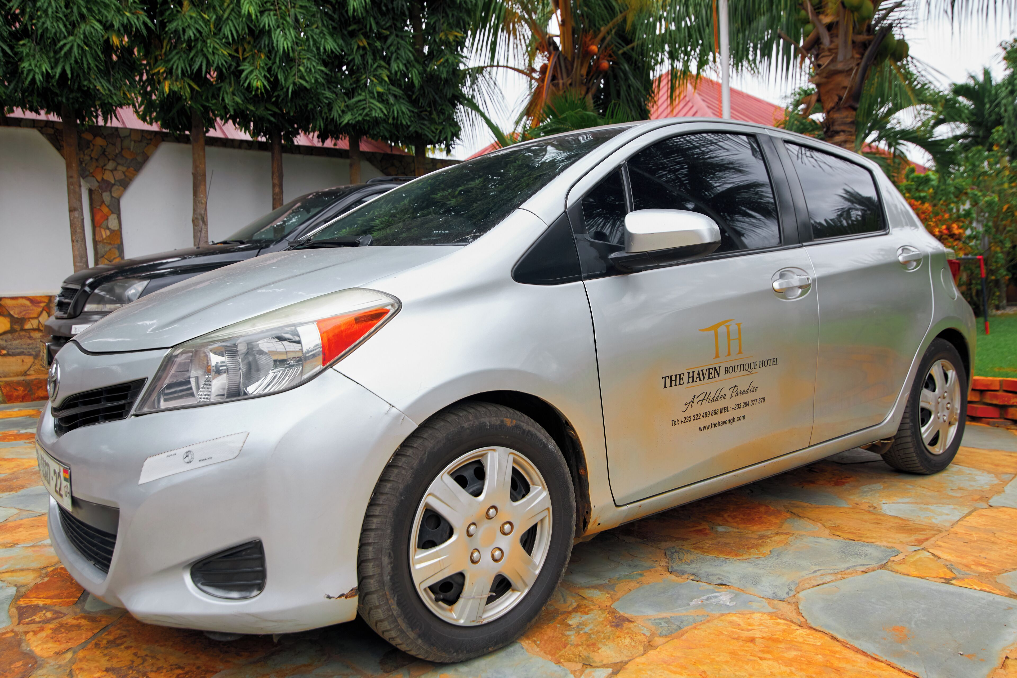 A silver hatchback car parked on a stone-paved area with a hotel sign on the side.