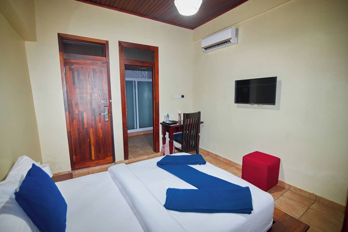 Una habitación de hotel con dos camas, un televisor, un taburete rojo y una puerta de madera.