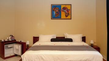 Une chambre d’hôtel avec un grand lit, une table de chevet en bois, un bureau avec une chaise et un tableau représentant deux cartes, accroché au mur.