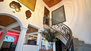 A spacious lobby with a wooden ceiling, a decorative staircase, and a large wall clock. - The Haven (Ejisu)