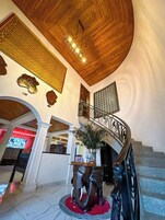 A spacious lobby with a wooden ceiling, a decorative staircase, and a large wall clock.