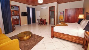 A hotel room with a wooden ceiling, a bed, a desk, a chair, a television, and a bathroom with a shower and toilet. - The Haven (Ejisu)