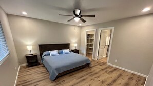 A bedroom with a bed, two bedside tables with lamps, a ceiling fan, and a walk-in closet.