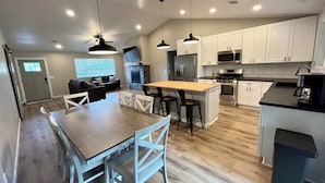 A modern kitchen with white cabinets, a central island, and a dining area with a wooden table and white chairs.