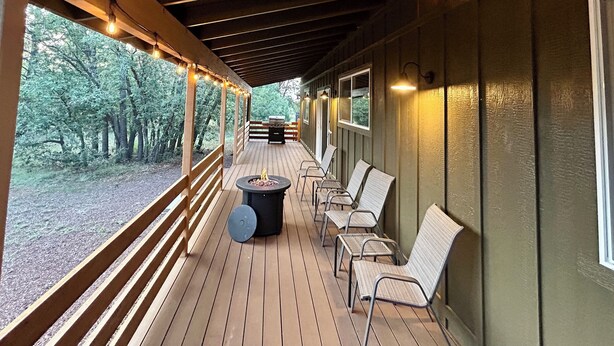 A covered deck with wooden railings, outdoor seating, and a fire pit.
