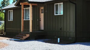 A single-story house with a dark green exterior, a chimney, a front door, and a small porch with steps.