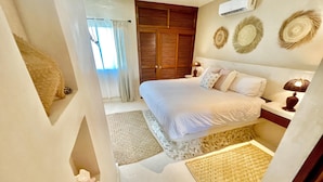 A bedroom with a bed, bedside tables, an air conditioning unit, and decorative wall art. - Mid-Island Condo with Rooftop Balcony (Isla Mujeres)