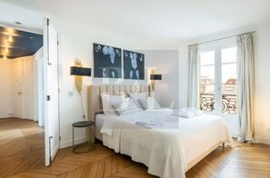Quarto com cama, mesa de cabeceira e janela com cortinas.